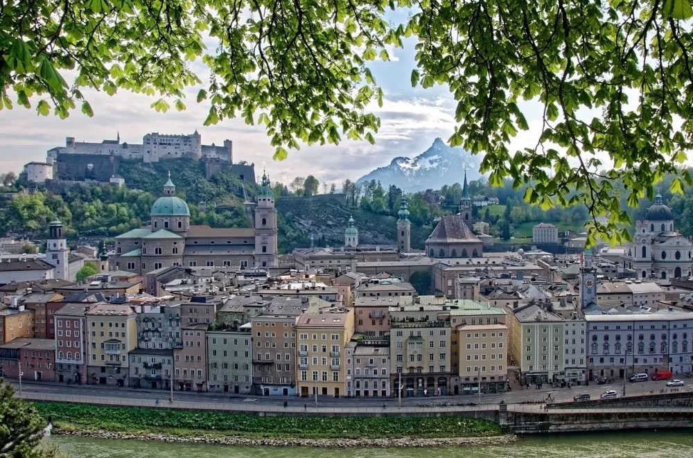 Entdecken Sie die malerische Aussicht auf Salzburg mit der majestätischen Festung Hohensalzburg, umgeben von historischen Gebäuden und der schönen Salzach. Diese atemberaubende Stadtansicht illustriert perfekt das kulturelle Erbe und die natürliche Schönheit Salzburgs, ideal für Kulturliebhaber und Reisende.