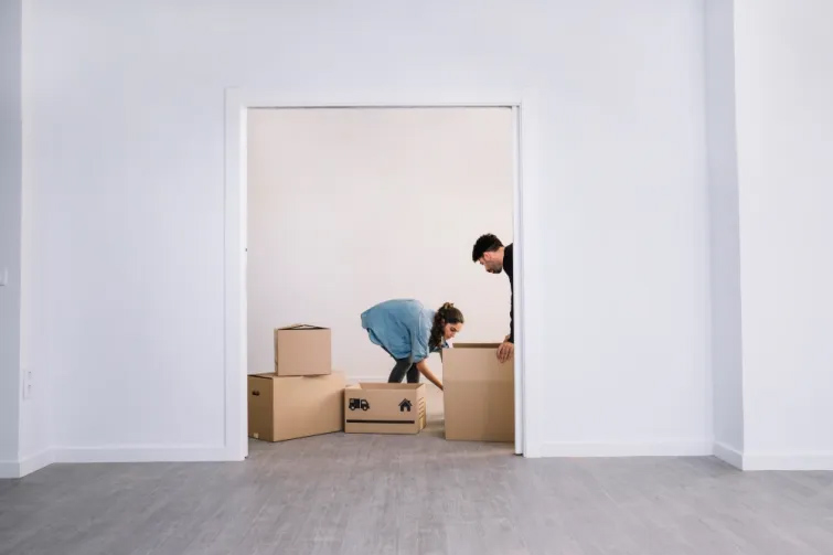 Ein junges Paar beim Umzug nach Linz: Sie packen gemeinsam Umzugskartons in ihrem neuen, leeren Wohnraum. Dieses Bild fängt den Beginn eines neuen Kapitels in Linz, der oberösterreichischen Landeshauptstadt, eingebettet in Kultur und Innovation, perfekt ein.
