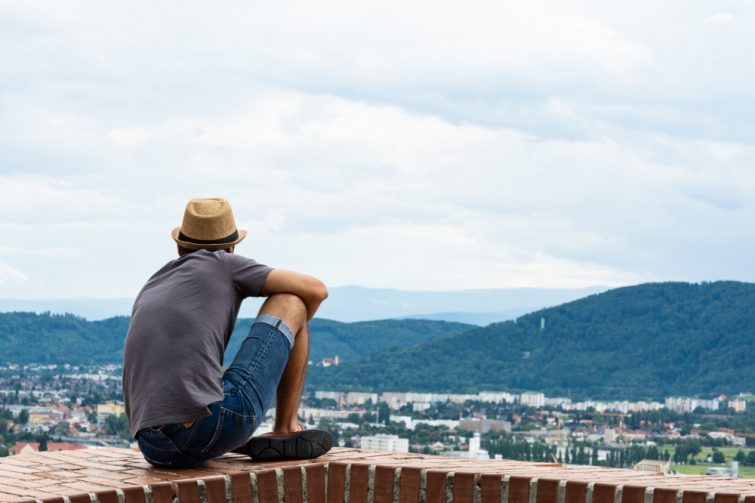 Ein Mann sitzt entspannt und genießt den Panoramablick über Graz, während er über die Aussichten und Möglichkeiten in der steirischen Hauptstadt nachdenkt. Dieses Bild symbolisiert Ruhe und Reflexion vor der malerischen Kulisse von Graz, ideal für zukünftige Bewohner und Besucher der Stadt.