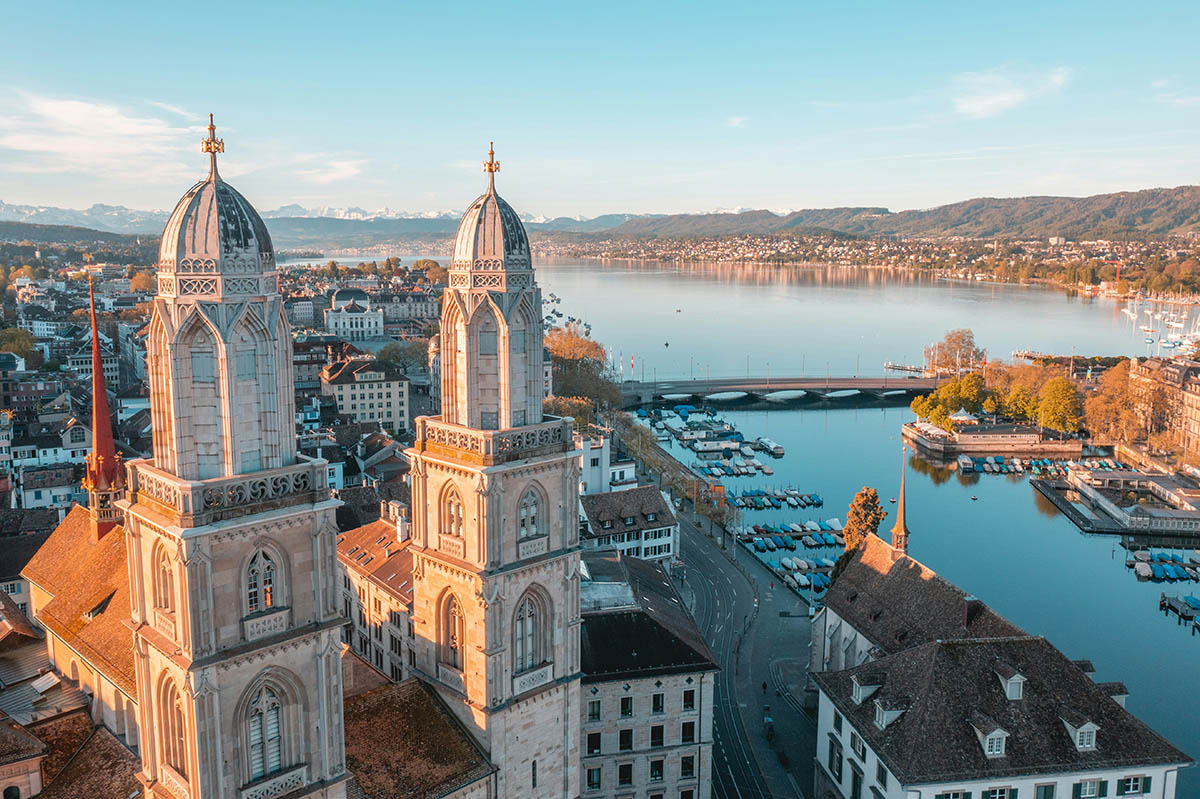 Entdecken Sie den atemberaubenden Blick auf Zürich mit seinen historischen Türmen der Großmünster Kirche, umgeben von der malerischen Kulisse des Zürichsees und den Schweizer Alpen. Ideal für Kultur- und Naturbegeisterte.